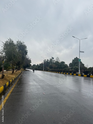 A tranquil perspective of a wide, empty wet road reflecting a gloomy overcast sky.