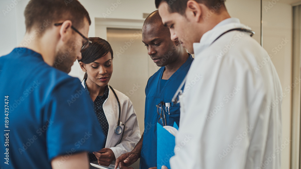 Obraz premium A diverse team of four doctors stands together in a hospital, deeply focused as they review medical documents. They all share a serious expression, reflecting the gravity of their discussion. 