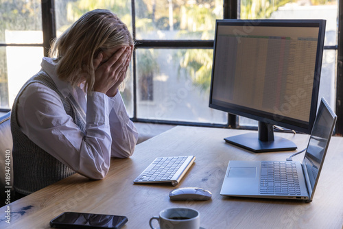 фотографія Woman at office desk burying face in hands beside wireless keyboard and monitor,