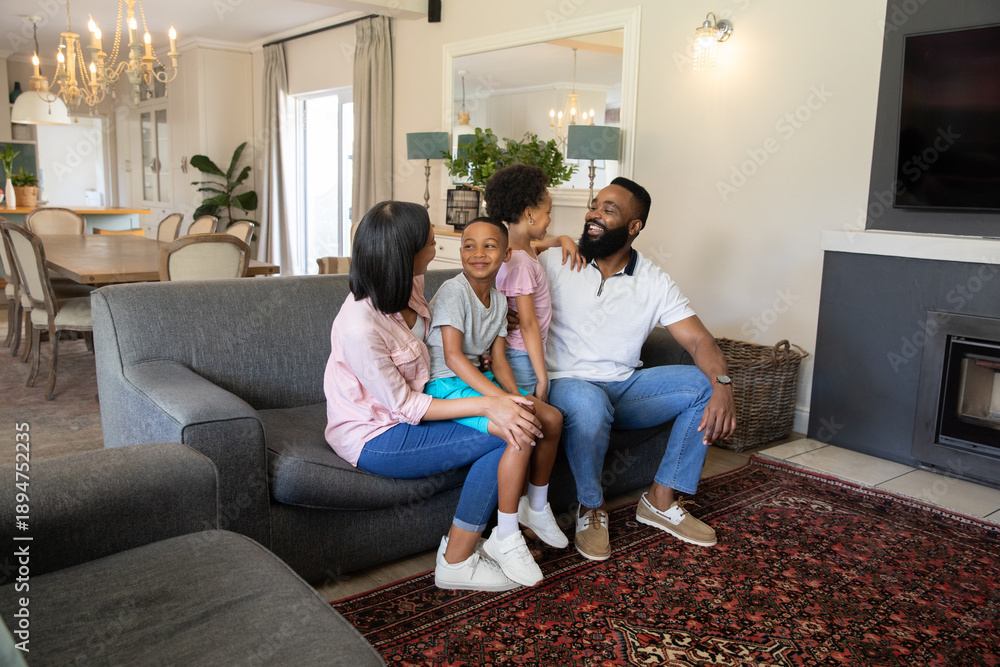 Fototapeta premium Diverse family sitting together on gray sofa over patterned red rug in bright living room