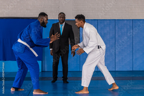 Canvas-taulu African american referee supervising judo competitors wearing uniforms for match