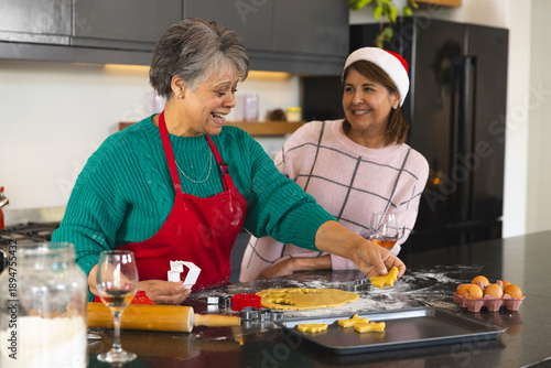 Senior mother and adult daughter cutting holiday cookie dough on counter with rolling pin, cutters