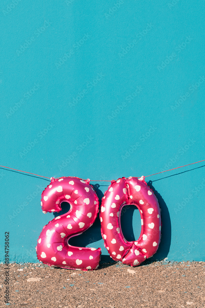Fototapeta premium pink number 20 balloons against a vivid blue wall