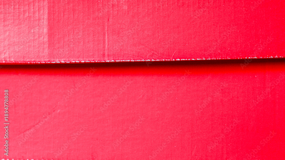 Fototapeta premium Red cardboard texture with a subtle ribbed surface and a bold horizontal shadow line from a box lid, vibrant full frame background with ample copy space