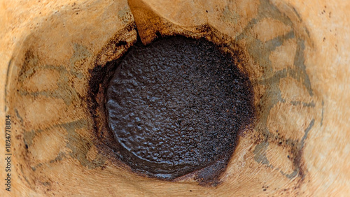 Coffee brewing process ending with wet espresso grounds in a paper filter, a close up top view showing residue and texture indicating morning ritual and caffeine preparation