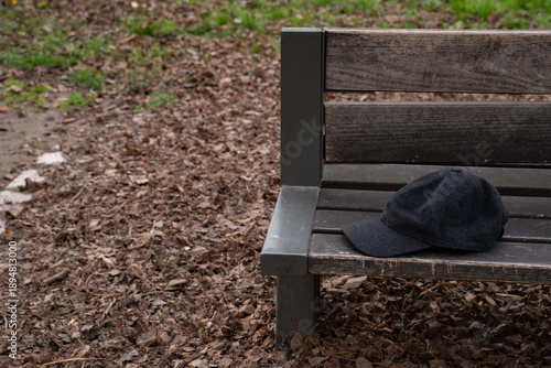 Black wool baseball cap resting on a wooden park bench outdoors. Everyday scene showing a personal accessory, representing casual style, leisure, and outdoor life.