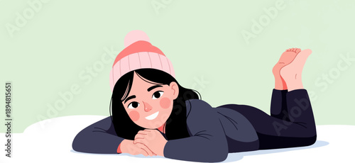 A smiling young girl in a winter hat and warm clothes relaxes in the snow