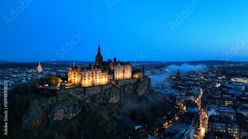 Illuminated castle on a hill overlooking city at dusk aerial view