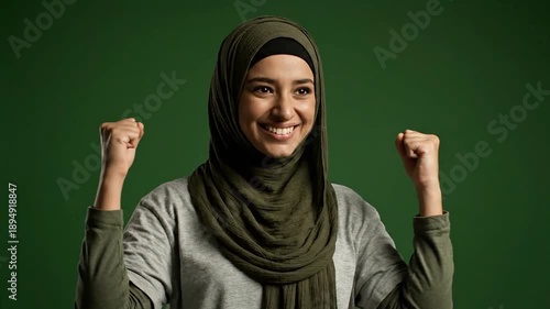 Woman in hijab celebrates with fists raised against a green background