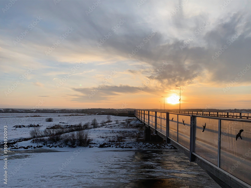 Obraz premium Winter sunset over the snow-covered Ihaste bridge and frozen Emajõgi River, Tartu, Tartumaa, Estonia, January 2021