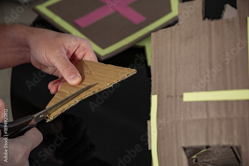 Male hands cutting cardboard crafts with scissors. Concept of DIY, handmade creativity, art therapy, craft making, imagination, and creative process at home.