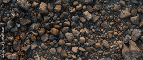 Overhead shot of a full frame textured background featuring uneven stones, cracks, and wet pebbles in daylight