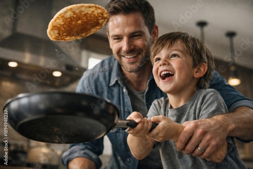 Happy father and young son flipping pancake in kitchen, fun family breakfast cooking moment at home.
