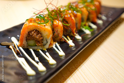 Gekkikara salmon rolls is a spicy sushi rolls filled with fresh salmon, spicy mayonnaise and cucumber. Delicious Japanese food served on a black ceramic plate.