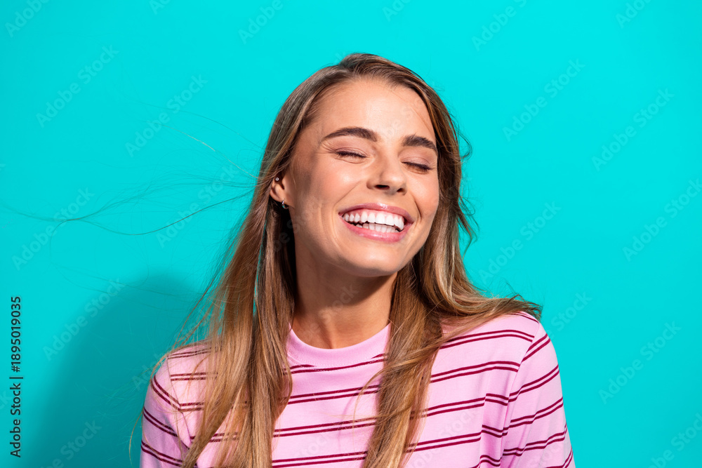 Fototapeta premium Cheerful young woman in striped pink shirt smiles with teal background lifestyle portrait