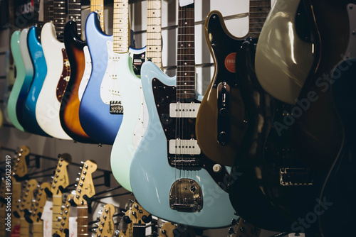 Many electric guitars hanging on wall of music shop, close up. Buying electric guitar. Stand with various colorful electric guitars in music shop.