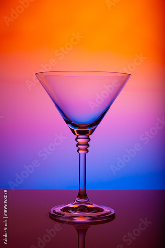 Clear martini glass with vivid purple orange blue gradient lighting, reflective tabletop, modern cocktail bar aesthetics, luxury glassware, minimal design, creative studio composition.