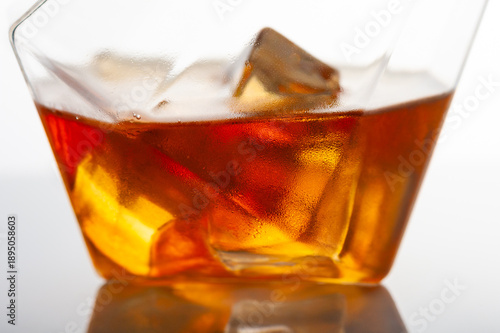 Cold whiskey cocktail with ice cubes in crystal glass, macro close up, amber alcohol drink texture, luxury bar beverage, refreshing drink concept, minimal studio background, selective focus.