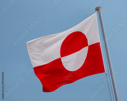 Greenland the Greenlandic national flag waving in the wind on a flagpole with blue sky background.