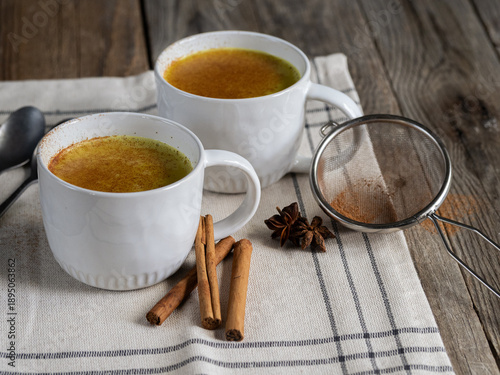 Two white cups of turmeric latte on rustic wooden table