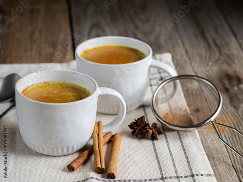 Two white cups of turmeric latte on rustic wooden table