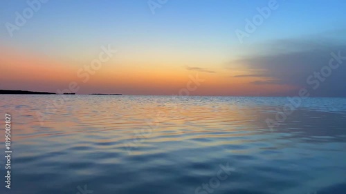 As the sun sets over Djerba beach in Tunisia, the sky transforms into beautiful shades of orange and blue, reflecting on the calm waters and creating a peaceful scenery.