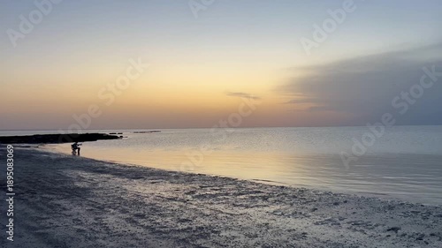 As the sun sets over Djerba beach in Tunisia, the sky transforms into beautiful shades of orange and blue, reflecting on the calm waters and creating a peaceful scenery.