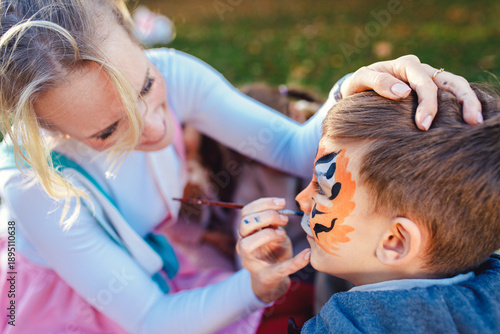 Female animator painting a child's face with a brush at an outdoor birthday party in a park.