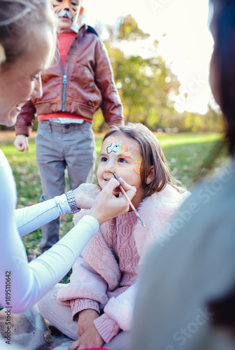 Billede på lærred Female animator painting a child's face with a brush at an outdoor birthday party in a park