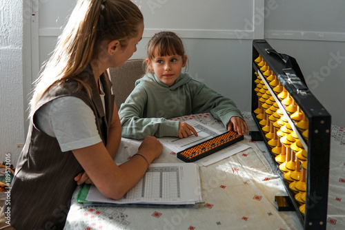 Eight year old girl learning mental arithmetic with abacus under teacher guidance, educational activity and childhood