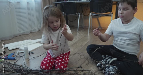 A creative family creates a craft from natural materials for a school project The mother son and daughter enjoy crafting, sitting on the floor and creating crafts from tree branches using a glue gun.