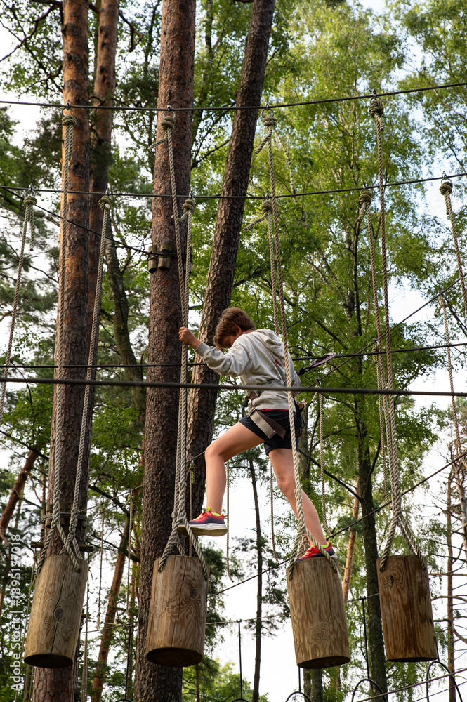 Obraz premium Active Boy Overcoming Rope Course Obstacles in Adventure Park