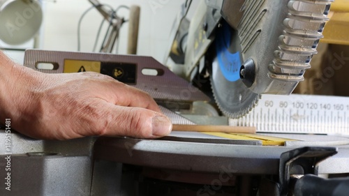 A close-up of a miter saw in action, a carpenter's hand holding a small round wooden dowel and sawing off a section on a miter saw with a sharp rotating blade