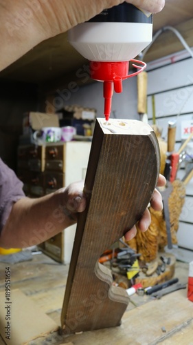 Male hands hold a bottle of glue and a wooden piece with holes and apply adhesive material to the cut for gluing wooden parts, joining parts of hard materials with wood glue