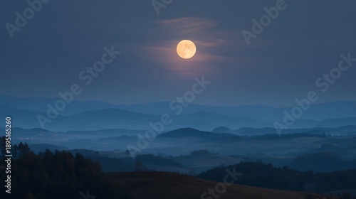 Full moon glowing in a deep twilight sky over silhouetted layers of blue misty hills and valleys.