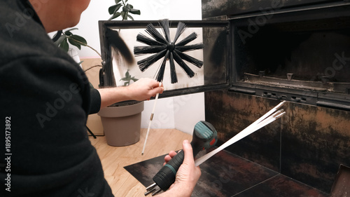 Man preparing to clean a modern indoor fireplace with a professional chimney brush.