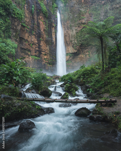 Aerial view of the dramatic Coban Rondo Waterfall cascading down rugged cliffs amidst a verdant jungle, Pujon, Jawa Timur, Indonesia.