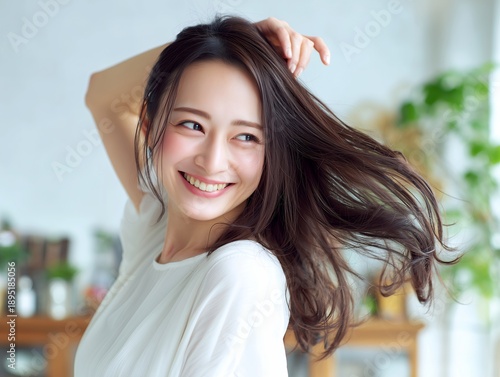 髪をかき上げて自然な動きと透明感ある笑顔が映える室内ポートレートの女性