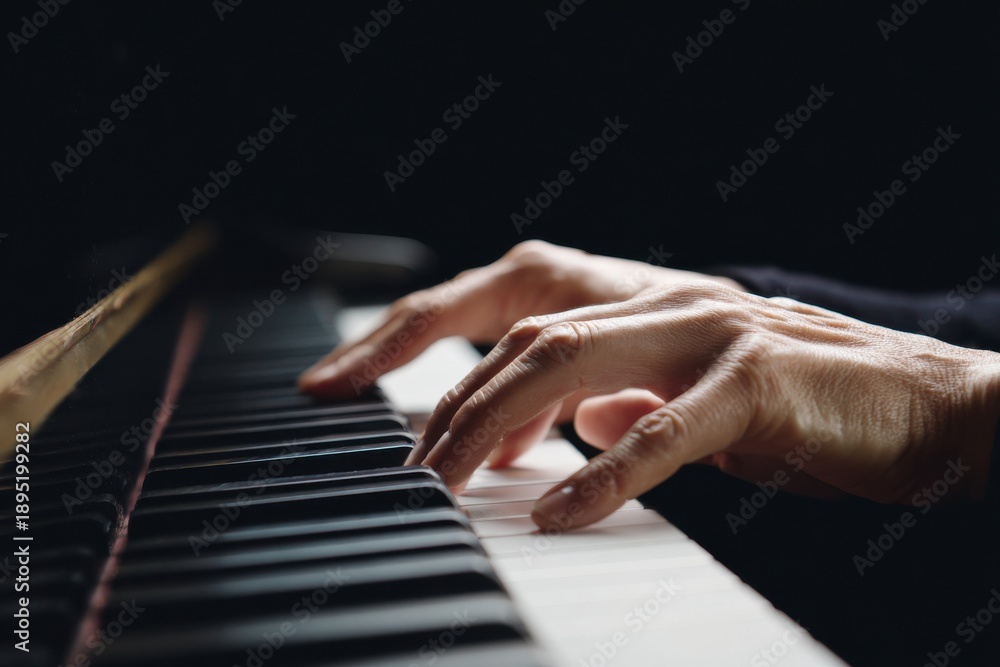 Fototapeta premium Close-up of caucasian female hands playing piano keys in low light