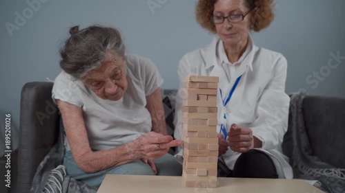 Mature doctor conducting session, therapy for senior patient in nursing home, training fine motor skills for dementia, alzheimer disease and recovery institute by folding wooden blocks, playing.