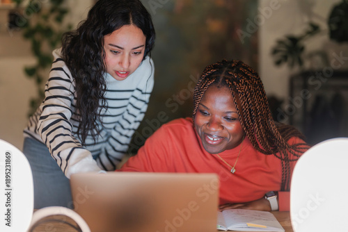 Two young women collaborate on a laptop, one pointing at the screen while the other smiles, engaged in learning or work.