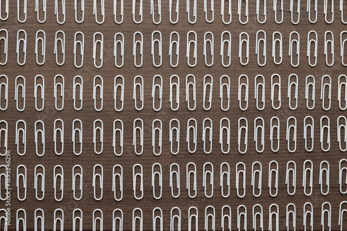 Many white paper clips on wooden table. Concepts of order obsession . Metaphor of ordinary people in society.