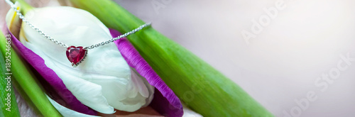 Banner of jewelry. Metal chain with stylish pink heart pendant on fresh flowers (tulip). It creating, tender, romantic atmosphere. Valentine's day, mother's, woman;s day, love holidays. Copy space.