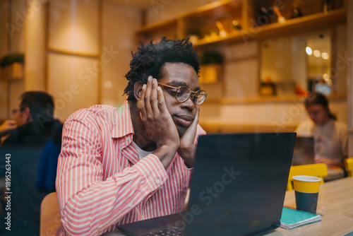 Quadro su tela Bored and disengaged young man rests his head on hands while staring at laptop screen