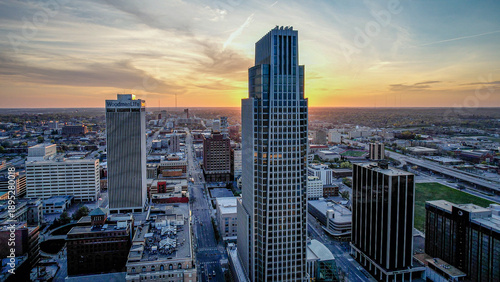 Aerial view of warm sunset hues paint the sky behind the First National Bank Tower and the Woodmen Tower, casting long shadows on the streets below, Omaha, Nebraska, United States.