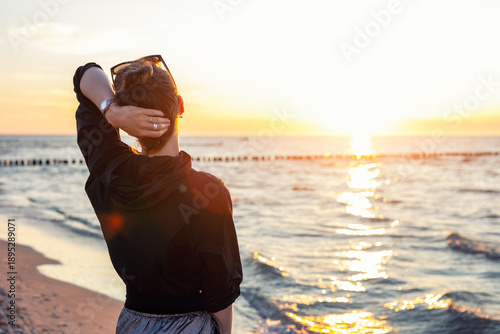 Fotografía Back view young adult woman dreamy looking sunset horizon on sandy beach shore warm evening sunset light