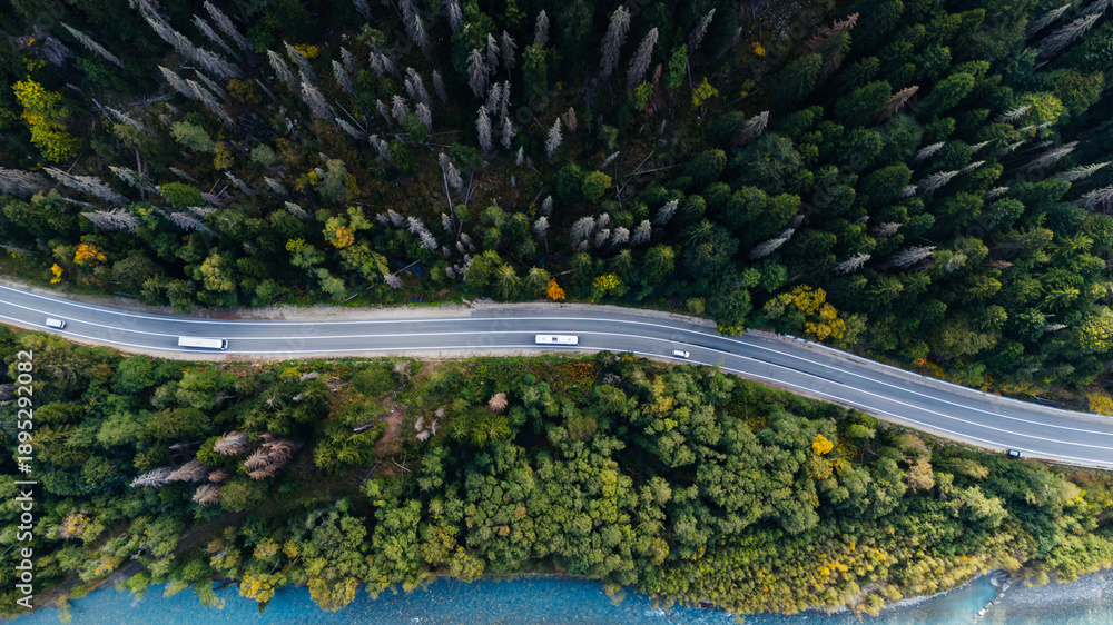 Fototapeta premium A car driving along a mountain road in an autumn forest, seen from a drone