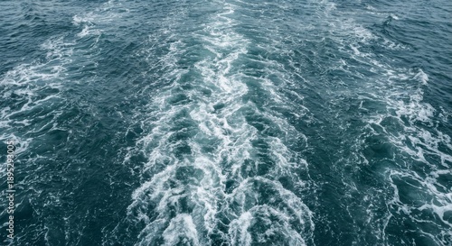 Turbulent white foamy wake from a ship churns the deep blue ocean surface, creating a dynamic trail of disturbed water with intricate patterns from a high angle view