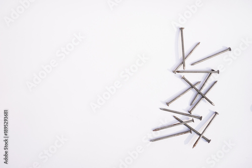 A pile of metal nails scattered on a white background casting shadows