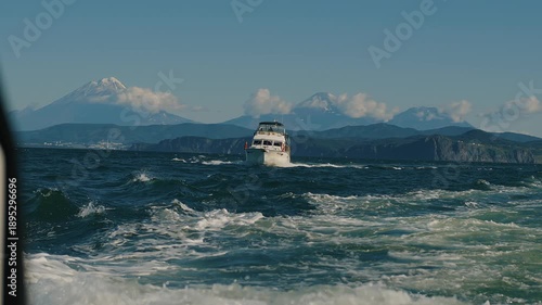 Kamchatka, Russia - August 26, 2025: Tourist-filled yachts depart from Avacha bay overlooking city on mountainous coast and volcanoes in clouds. Travel and tourism concept